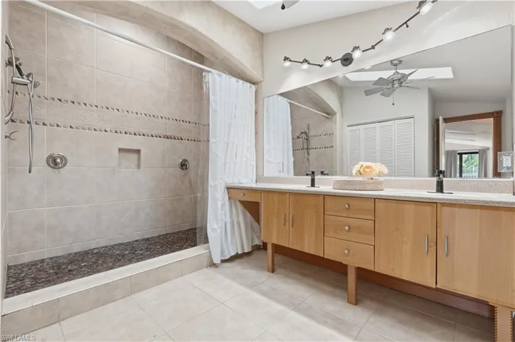 Bathroom with double vanity, a tile shower, a ceiling fan, and light tile patterned flooring
