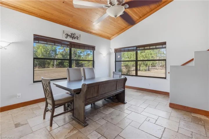 Dining space with stone tile flooring, wood ceiling, a ceiling fan, high vaulted ceiling, and a desk
