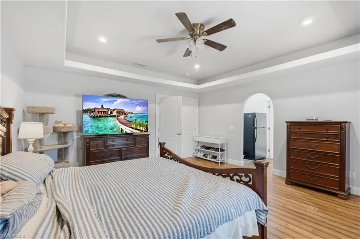 Bedroom featuring freestanding refrigerator, ceiling fan, hardwood / wood-style flooring, arched walkways, and a tray ceiling