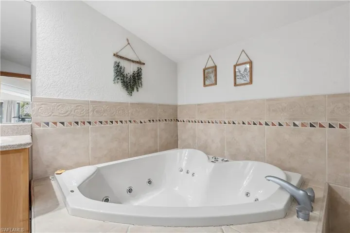 Bathroom featuring a tub with jets, a textured wall, vanity, and lofted ceiling