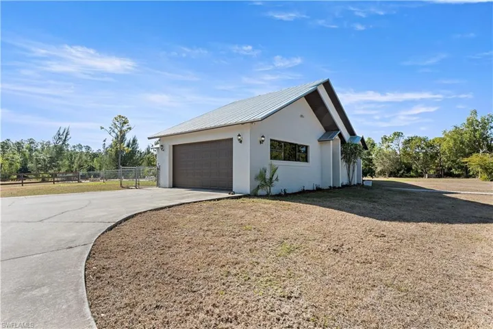 View of property exterior featuring a metal roof, stucco siding, a garage, concrete driveway, and an outbuilding