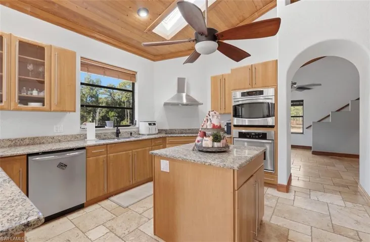 Kitchen featuring glass fronted cabinets, a vaulted wood ceiling, stone tile floors, a skylight, and a ceiling fan
