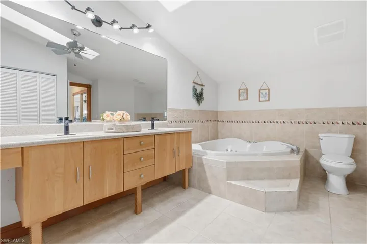 Full bathroom featuring double vanity, a bath, a skylight, light tile patterned floors, and tile walls