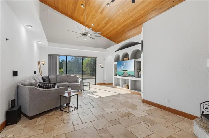 Living area featuring built in shelves, stone tile flooring, ceiling fan, high vaulted ceiling, and wooden ceiling
