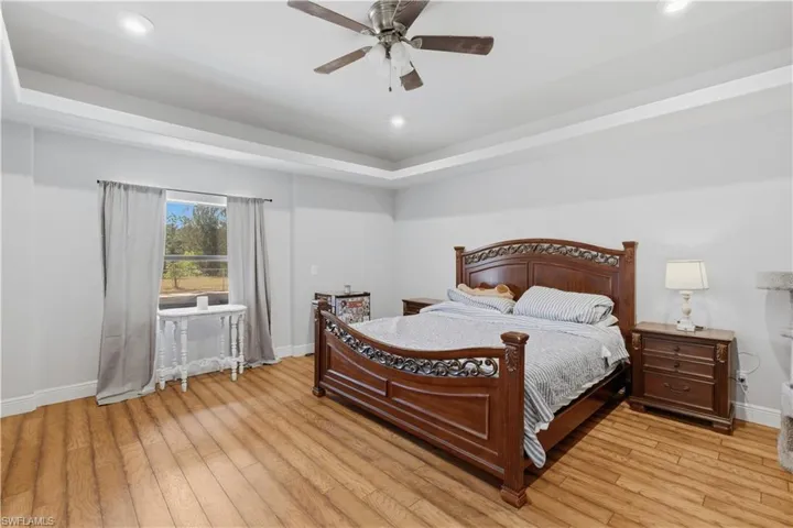 Bedroom featuring a raised ceiling, ceiling fan, recessed lighting, and light wood-style flooring