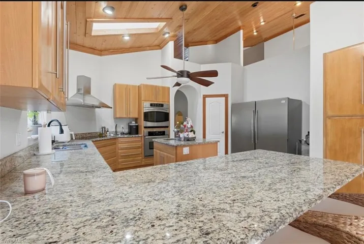 Kitchen with a skylight, light stone counters, stainless steel appliances, a vaulted wood ceiling, and a kitchen bar
