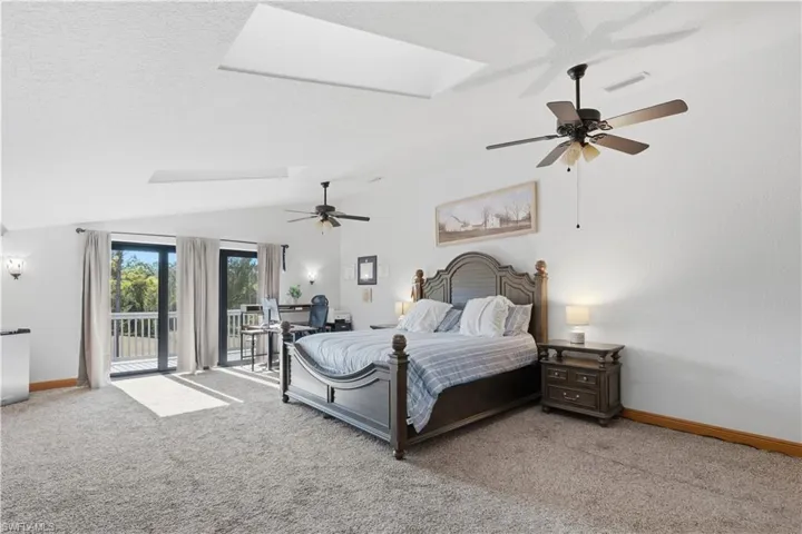 Bedroom with carpet, access to exterior, ceiling fan, a skylight, and lofted ceiling