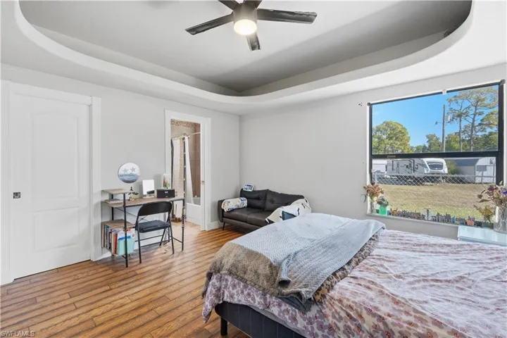 Bedroom featuring a tray ceiling, hardwood / wood-style floors, a ceiling fan, and ensuite bathroom