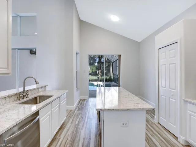 Kitchen featuring Quartz counters, white cabinetry, dishwasher, vaulted ceiling, and light wood-type flooring