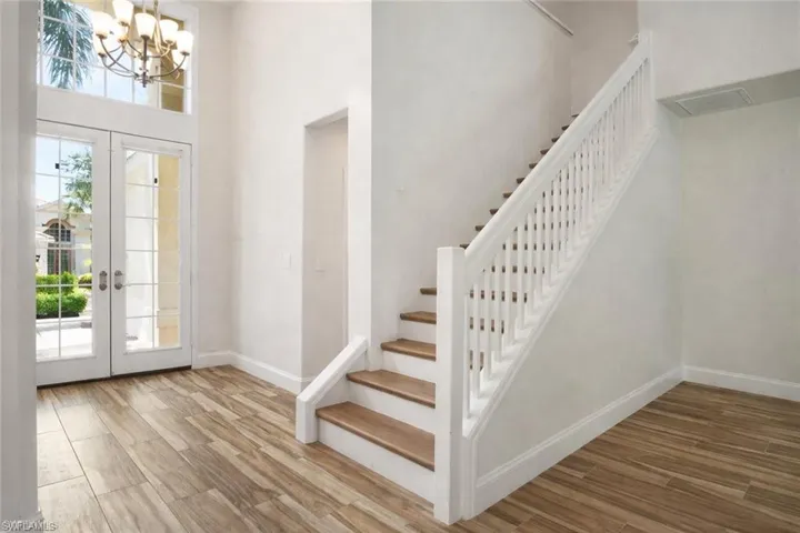 Foyer with wood tiled floors, french doors with retractable blinds, vaulted ceiling, and chandelier