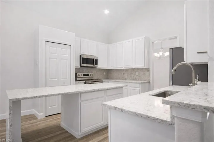 Kitchen featuring lofted ceiling, light stone counters, white cabinets, stainless steel appliances, and light wood-style flooring