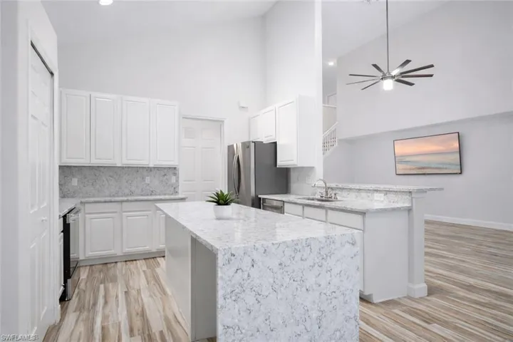 Kitchen with light wood-style flooring, light quartz countertops,vaulted ceiling, and white cabinets