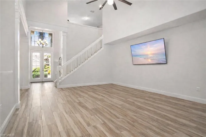 Unfurnished living room with a high ceiling, light wood-style flooring, a ceiling fan, hanging lights, and french doors