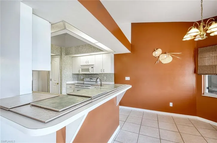 Kitchen featuring hanging light fixtures, light tile patterned floors, an inviting chandelier, electric stove, and white cabinets
