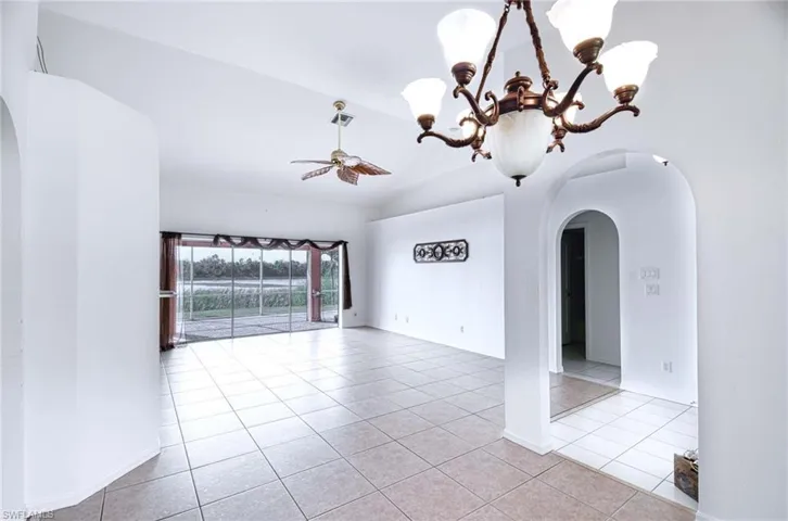Tiled empty room with lofted ceiling and ceiling fan with notable chandelier