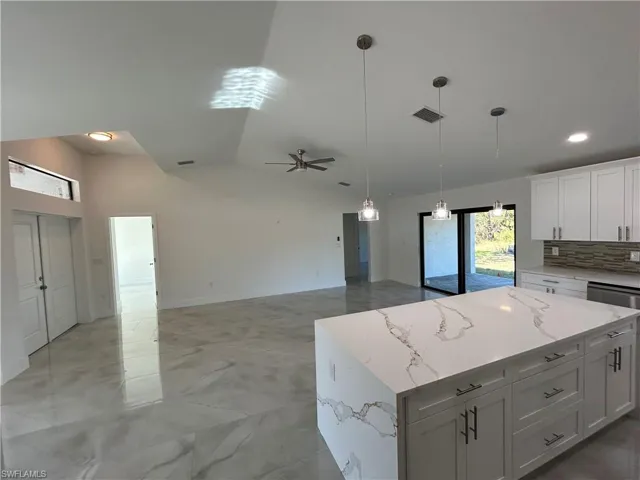 Kitchen with white cabinetry, a kitchen island, light stone countertops, and ceiling fan