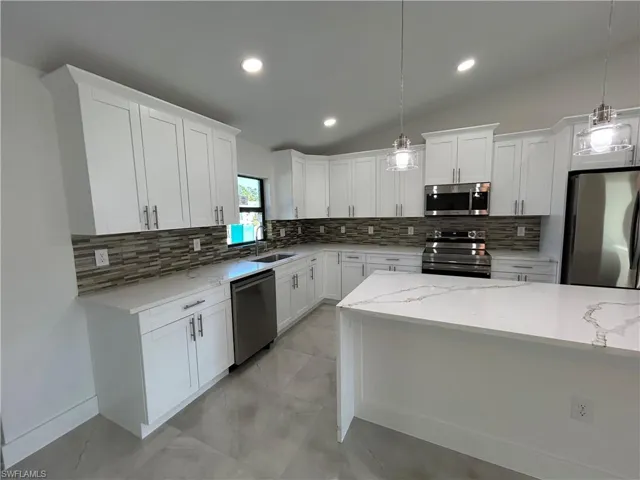 Kitchen with white cabinets, decorative light fixtures, appliances with stainless steel finishes, and vaulted ceiling
