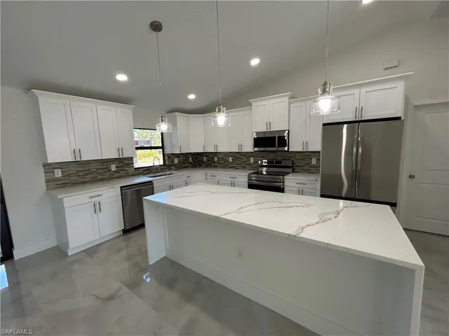 Kitchen with appliances with stainless steel finishes, vaulted ceiling, pendant lighting, white cabinets, and a center island