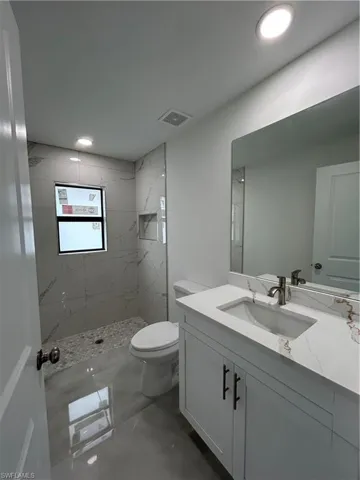 Bathroom with toilet, tiled shower, and vanity