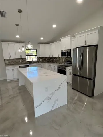 Kitchen with stove, lofted ceiling, refrigerator, decorative light fixtures, and a kitchen island