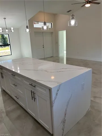 Kitchen with light stone countertops, white cabinetry, hanging light fixtures, and lofted ceiling