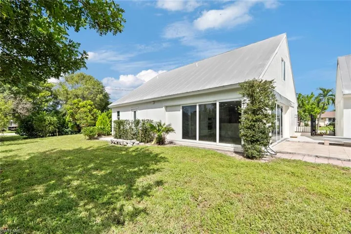 White stucco exterior featuring a gabled metal roof, large sliding glass doors, a patio and a grassy yard