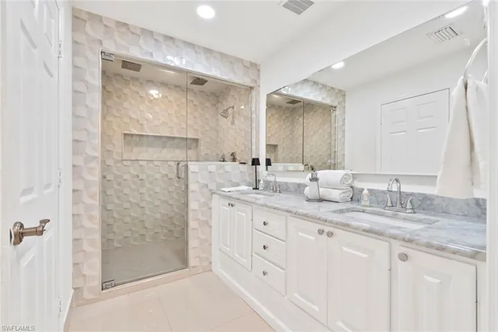 Dual vanity with stone countertop, frameless glass shower enclosure, textured tile shower surround