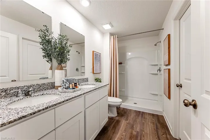 Photos are of a model home or artist rendering. Home may be virtually staged; Bathroom with vanity, a textured ceiling, wood-type flooring, toilet, and a shower with curtain