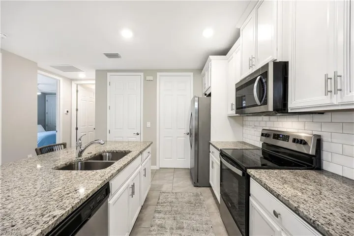 Kitchen with appliances with stainless steel finishes, white cabinets, light stone counters, tasteful backsplash, and light tile patterned floors