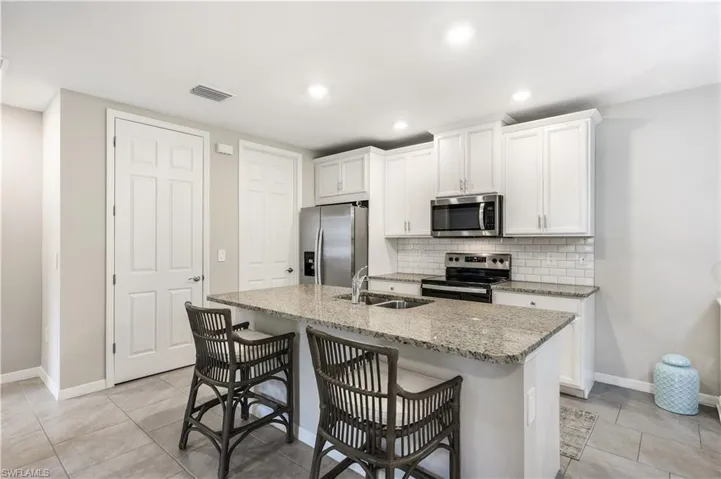 Kitchen featuring light stone counters, stainless steel appliances, white cabinetry, a breakfast bar area, and tasteful backsplash