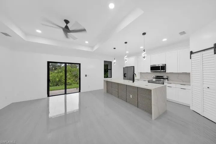 Kitchen featuring white shaker-style cabinetry, an oversized island with a slatted wood-finish base and stone-surface countertop, recessed lighting, pendant fixtures, and large-format tile flooring