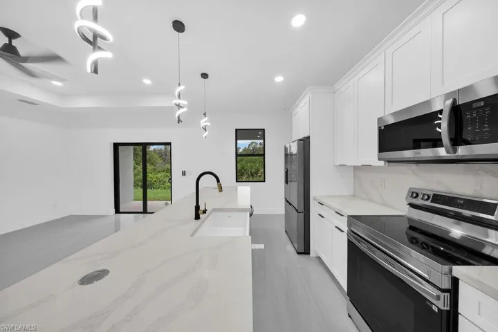 Kitchen featuring white shaker-style cabinetry, a large central island with a quartz countertop, a matte black high-arch faucet, stainless steel appliances, and contemporary spiral pendant lighting