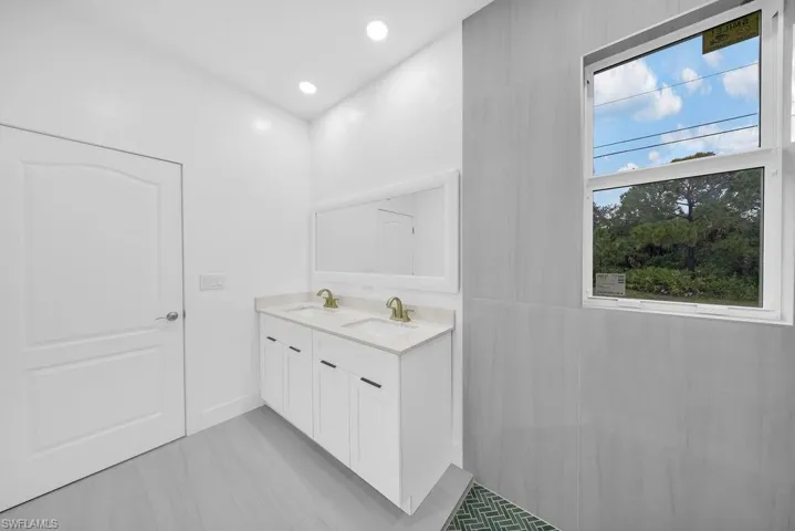 Double vanity with white cabinetry, quartz countertop, brass-toned fixtures, and a wall-to-wall mirror, complemented by large-format gray wall tiling