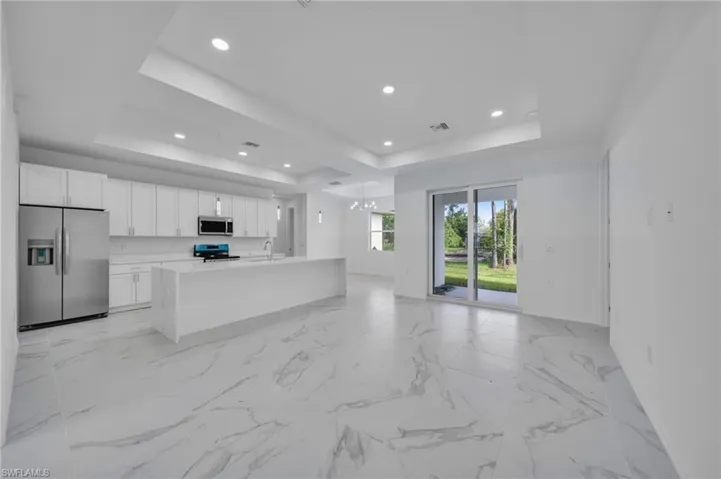Kitchen featuring stainless steel appliances, open floor plan, white cabinetry, an island with sink, and light stone counters