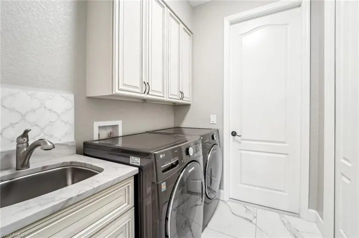 Utility room featuring a built-in sink with a gooseneck faucet, marble-look countertop, white shaker-style cabinetry, and white paneled door with dark hardware