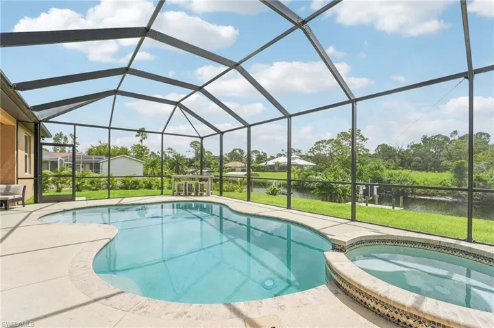 Screen-enclosed pool area featuring a freeform swimming pool, integrated spa with mosaic tile detailing, and a spacious concrete deck