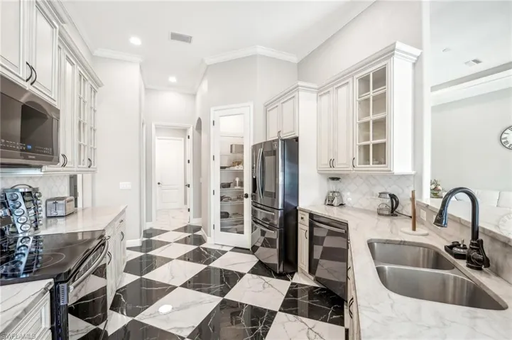 Kitchen featuring black and white checkerboard flooring, light-toned cabinetry, stainless steel appliances, a double basin sink with a gooseneck faucet, and an integrated pantry with a glass-paneled door