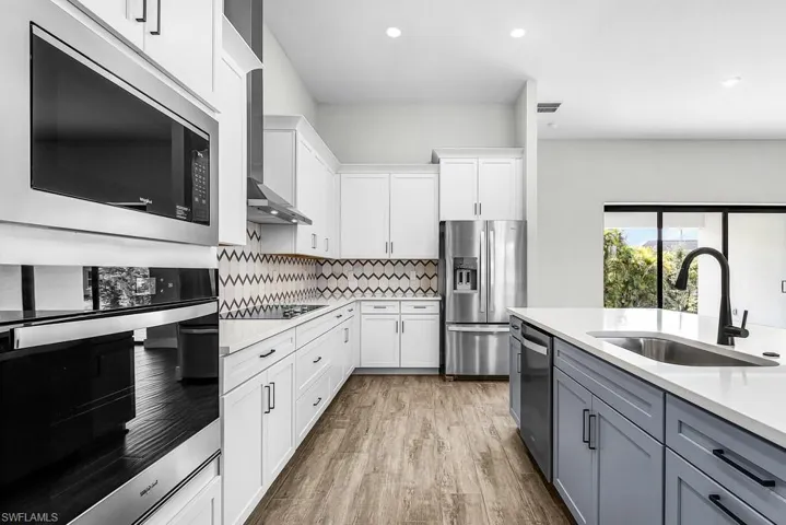 Kitchen featuring stainless steel appliances, dual tone cabinetry, light wood finished floors, light stone countertops, and recessed lighting