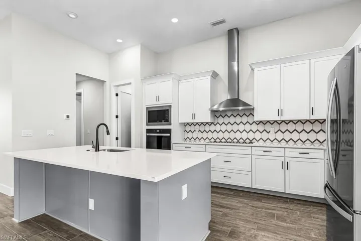 Two tone kitchen featuring wood tiled floors, stainless steel appliances, a center island with sink, light stone countertops, and tasteful backsplash