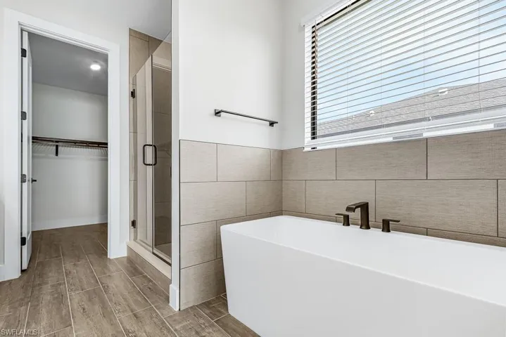 Bathroom with a stall shower, a freestanding tub, wood tiled floors, a spacious closet, and tile walls
