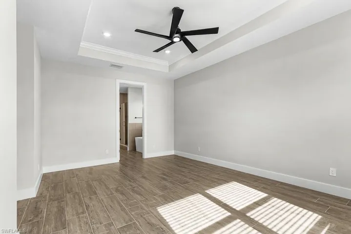 Empty room with wood tiled floors, crown molding, recessed lighting, a ceiling fan, and a tray ceiling