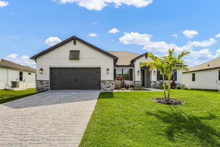 View of front of house with stucco siding, a front yard, and decorative driveway