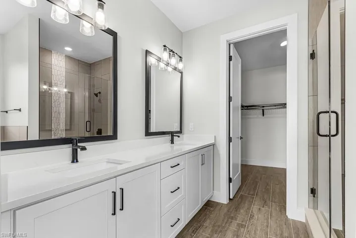 Full bath with a stall shower, double vanity, wood finish floors, a spacious closet, and recessed lighting