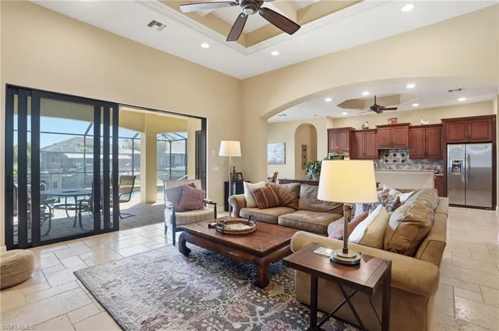 Living area with ceiling fan, stone tile floors, arched walkways, a tray ceiling, and recessed lighting