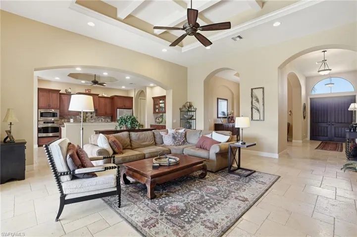Living area featuring a ceiling fan, stone tile flooring, coffered ceiling, recessed lighting, and arched walkways