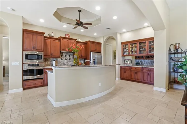 Kitchen featuring arched walkways, stainless steel appliances, a tray ceiling, glass fronted cabinets, and crown molding