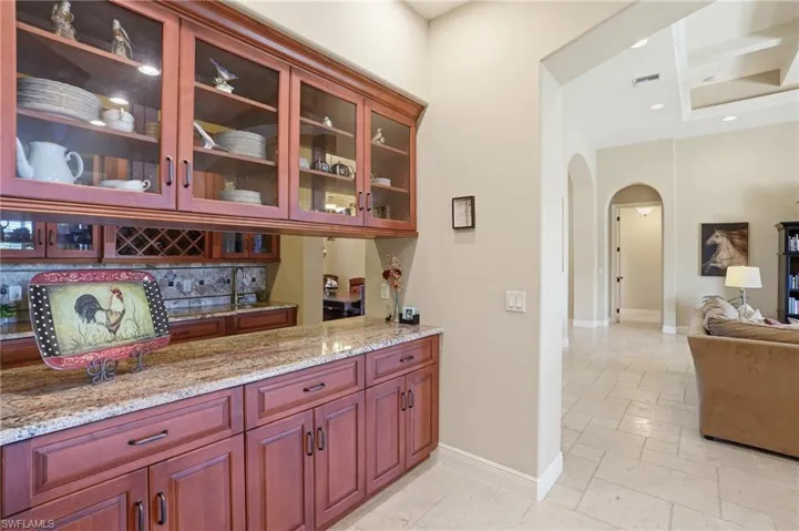 Bar featuring arched walkways, glass insert cabinets, light stone counters, recessed lighting, and tasteful backsplash