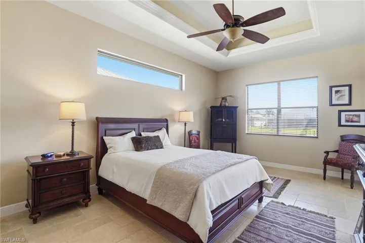 Bedroom featuring ceiling fan, a raised ceiling, stone tile flooring, and crown molding