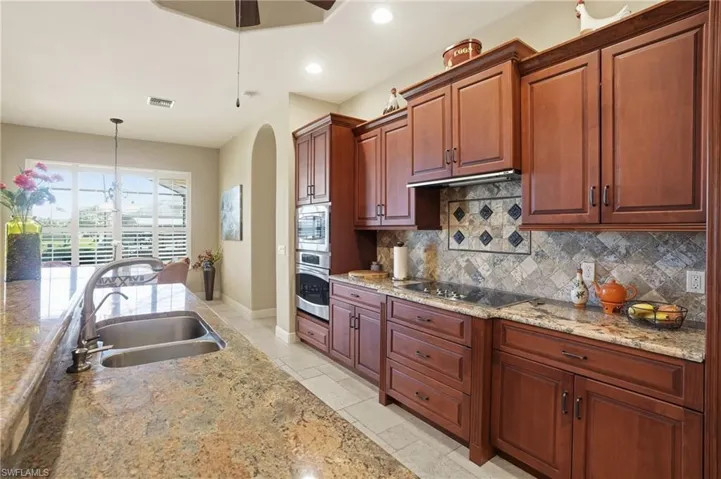 Kitchen with light stone counters, arched walkways, stainless steel appliances, and a ceiling fan