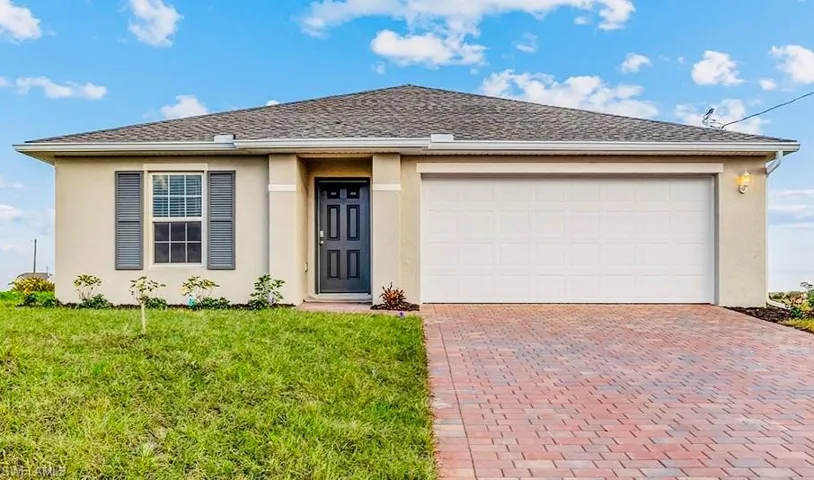 View of front facade with decorative driveway, stucco siding, a front lawn, and a garage